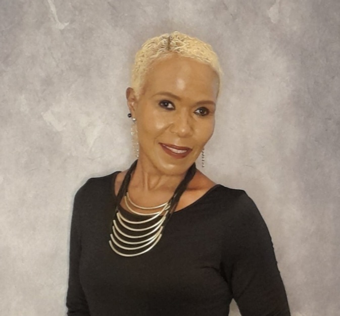 Bree Theodore standing with a gentle smile in front of a gray backdrop